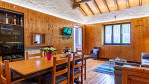 Ein Zimmer mit Holzwänden, einem Esstisch, Stühlen, einem Fernseher und einem Sofa.