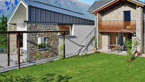 Una casa moderna con fachada de piedra, techo de metal y una escalera que conduce a una terraza de madera.