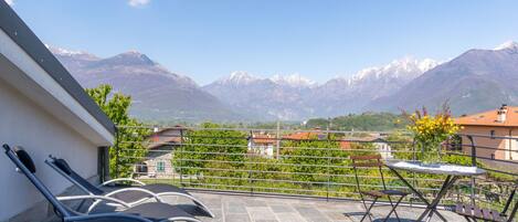 A balcony with a view of mountains, a table with a vase of flowers, and two lounge chairs.