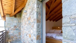 A stone-walled room with a wooden ceiling, a bed with white bedding, and a small window. - Baila (CCO510) by Interhome (Colico)