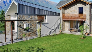 A modern house with a stone facade, a metal roof, and a staircase leading to a wooden deck. - Baila (CCO510) by Interhome (Colico)