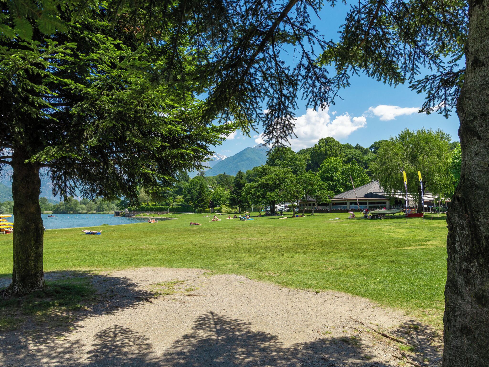 A park with a lake, trees, and a building with a roof.