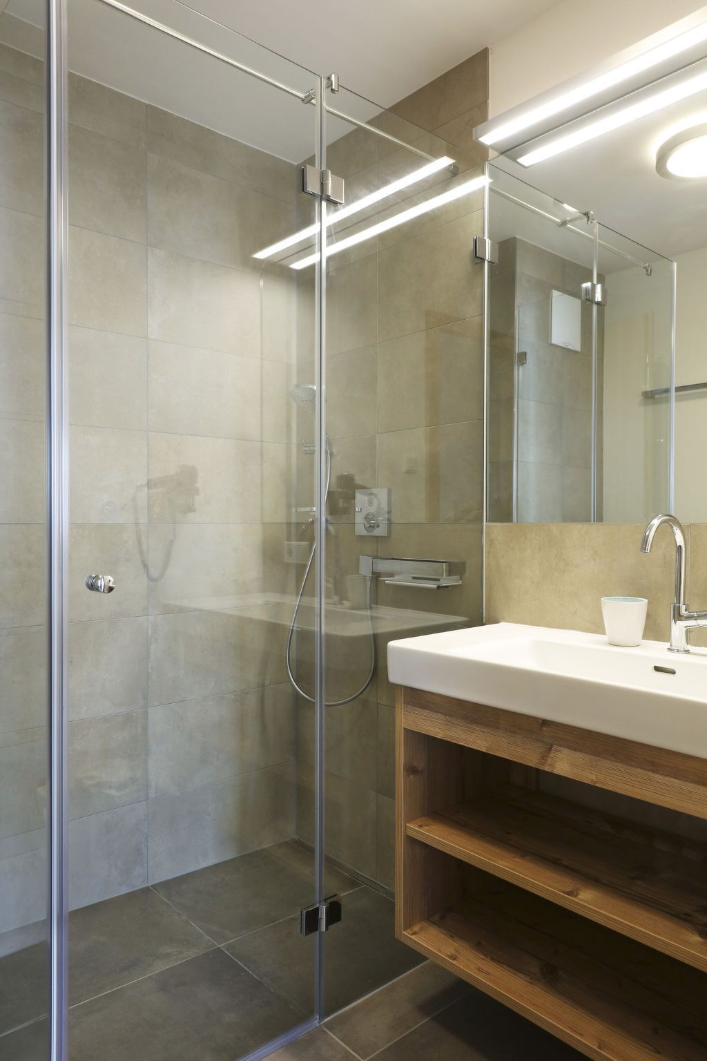 A modern bathroom with a glass-enclosed shower, a wooden vanity, and a large mirror.