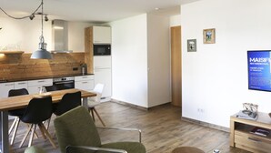 Eine moderne Küche mit weißen Schränken, einer Holzausziehtafel und einer Pendelleuchte. Es gibt einen Essbereich mit einem Holztisch und Stühlen.