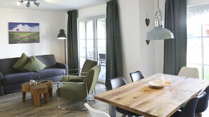 Ein modernes Wohnzimmer mit Sofa, Sesseln, einem Esstisch und einem Gemälde an der Wand.