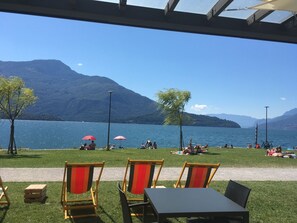 Área externa com mesas e cadeiras, com vista para um lago e montanhas ao fundo.