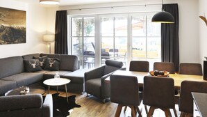 Un salon moderne avec un canapé, une table basse et un coin repas. On y trouve une grande fenêtre avec des rideaux, un tableau au mur et une lampe.