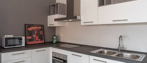 A modern kitchen with white cabinets, a stainless steel sink, a microwave, and an oven.