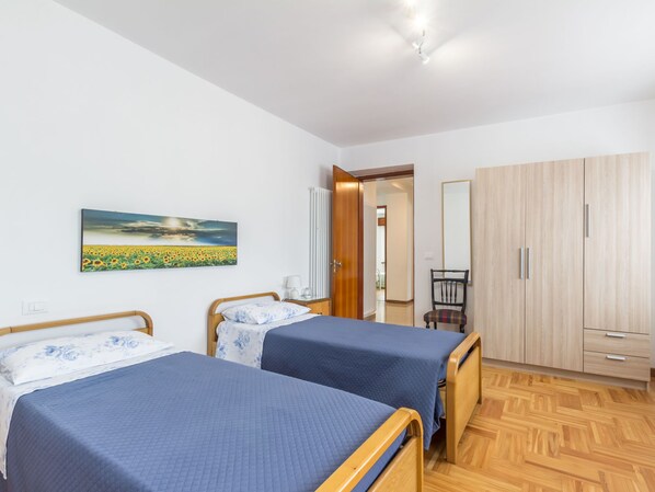A bedroom with two beds, a wooden wardrobe, a chair, and a painting of a sunflower field.