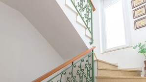 Een trap met groene metalen leuningen en houten handlijsten, die uitkomt op een plateau met een potplant.