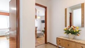 Een gang met een houten deur, een houten console en een vaas bloemen, en een spiegel aan de muur.