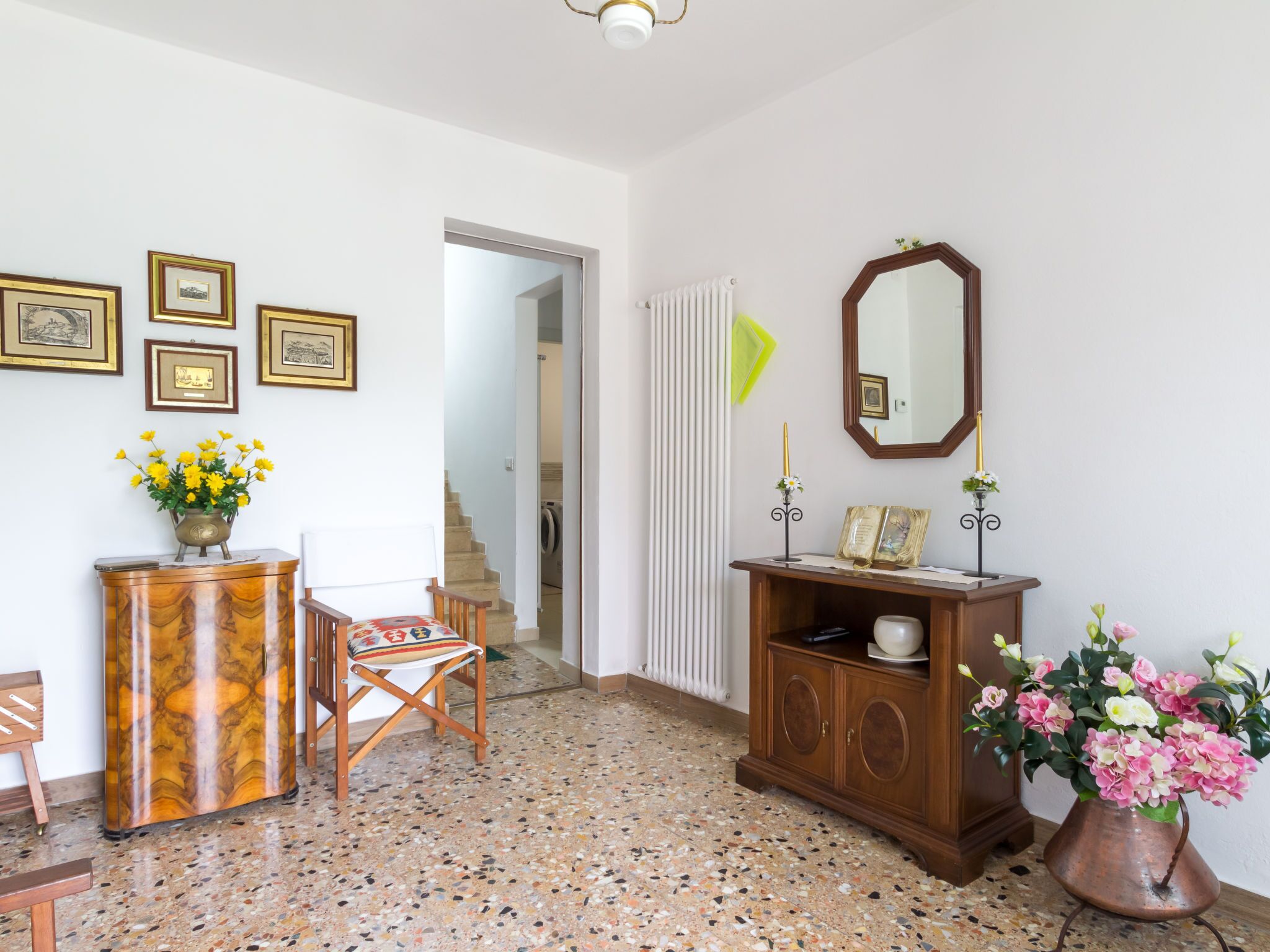 Un couloir avec une armoire en bois, une chaise, un miroir et un escalier menant à une autre pièce.