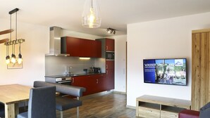 Un soggiorno moderno con zona pranzo, cucina e TV che mostra una pubblicità di un parco acquatico.