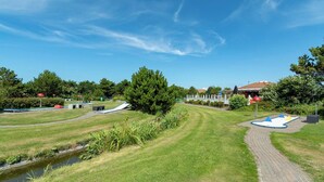A grassy area with a paved path, a small water channel, and a playground with climbing structures. - Apartment in Julianadorp by the Sea (Julianadorp aan Zee)