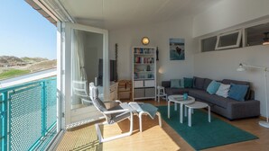 A balcony with a view of the landscape, a sofa, a bookshelf, and a dining area. - Apartment in Julianadorp by the Sea (Julianadorp aan Zee)