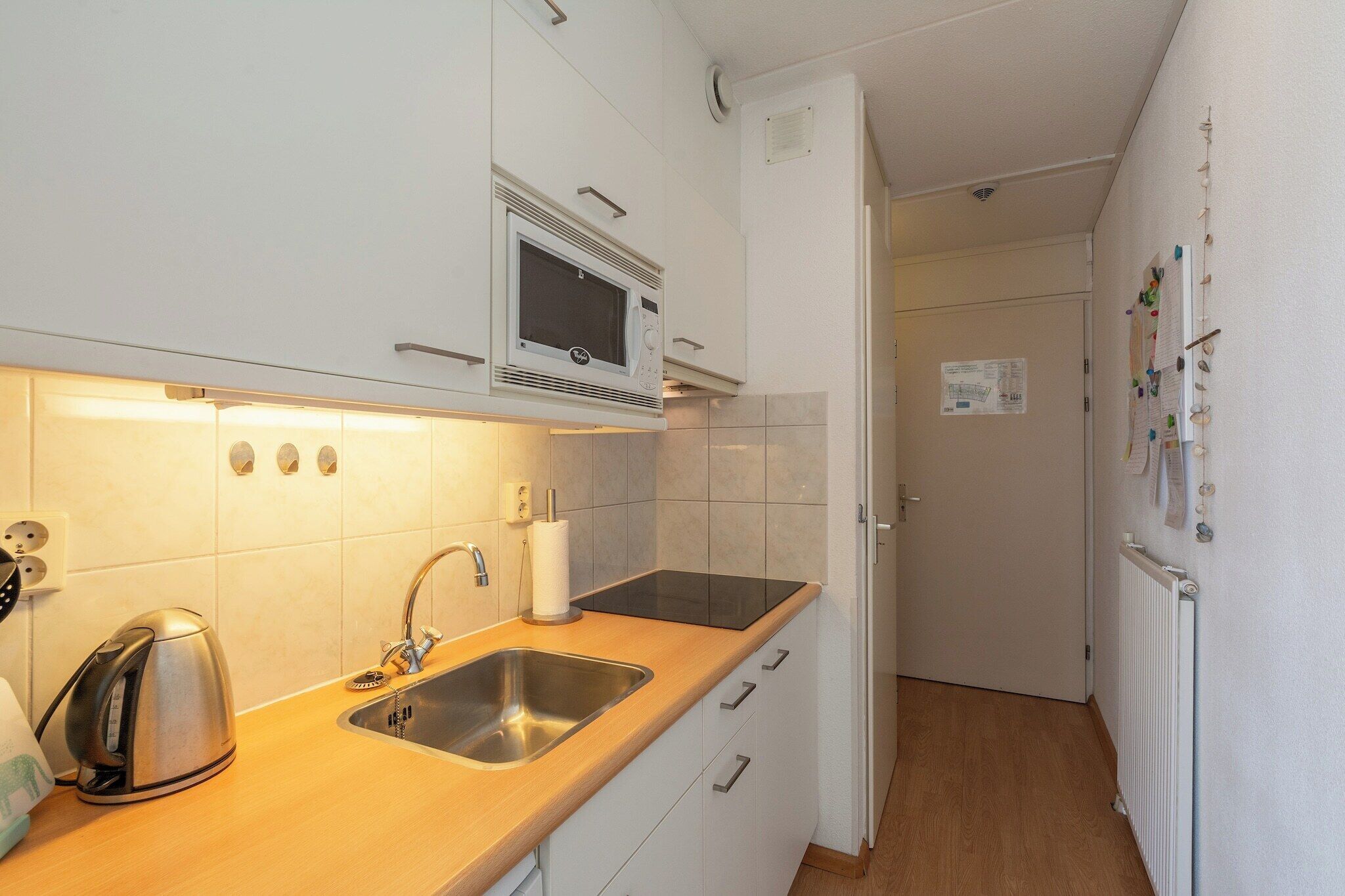 A compact kitchen with a microwave, kettle, sink, and white cabinets.