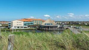 A waterfront hotel with a central round building, a modern building with orange roofs, and a body of water in the foreground. - Apartment in Julianadorp by the Sea (Julianadorp aan Zee)