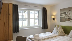 Une chambre d’hôtel avec deux lits, un bureau, une chaise, une fenêtre avec des rideaux, une lampe fixée au mur et un tableau.