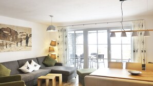 Un salon moderne avec un canapé, une table basse et un coin repas. Il y a une grande fenêtre avec des rideaux, un tableau au mur et une lampe.
