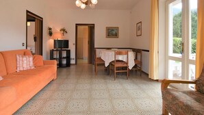 Een woonkamer met een bank, een tv-meubel, een eettafel met stoelen en een groot raam met gordijnen.