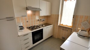A compact kitchen with white cabinets, a gas stove, a built-in oven, and a window with a curtain.