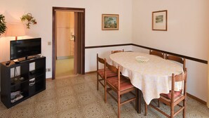 A dining area with a table and chairs, a television on a stand, and a door leading to another room. - Villa Laura by Interhome (Lago d'Idro)