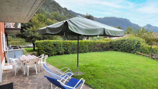 An outdoor patio with a table and chairs, a covered umbrella, and a view of mountains. - Villa Laura by Interhome (Lago d'Idro)