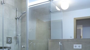 Une salle de bain moderne avec une douche à l’italienne en verre, un lavabo blanc avec une serviette et un miroir au-dessus du lavabo.