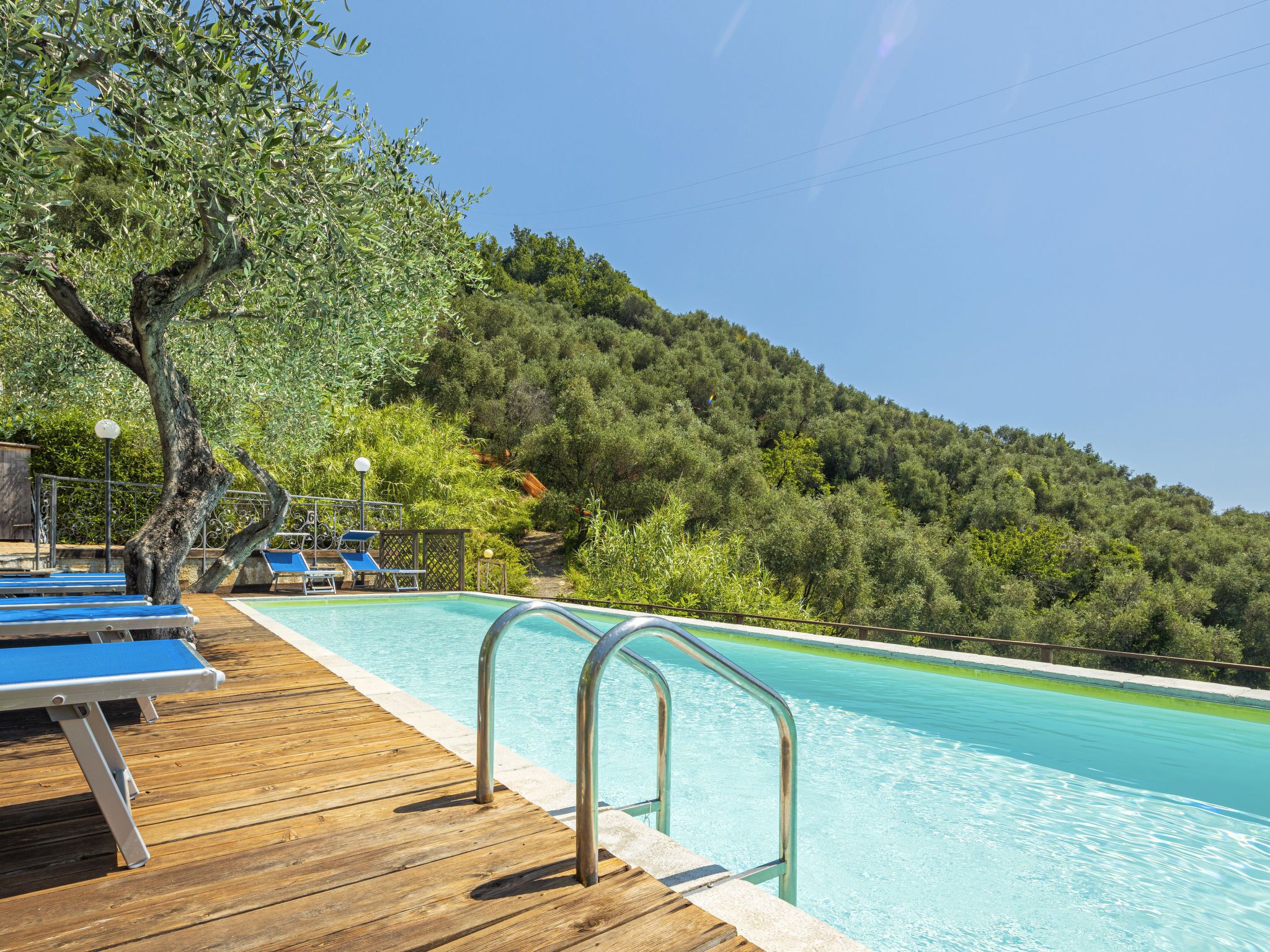 A wooden deck with blue lounge chairs and a swimming pool with metal railings.