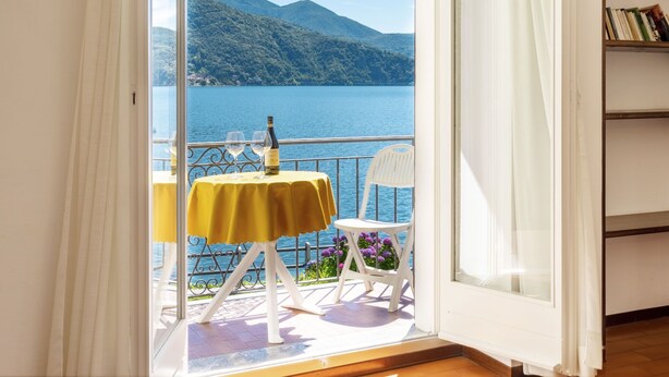 Ein Zimmer mit Balkon und Blick auf einen See, ein Tisch mit einer Flasche und ein Stuhl.