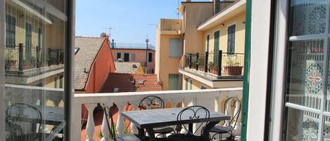 A balcony with a table and chairs, overlooking a row of buildings with red-tiled roofs.