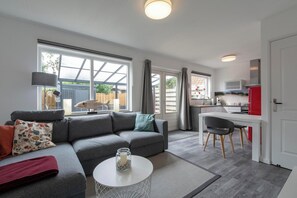 A modern living room with a grey sofa, a small round table, and a kitchen area with a red fridge and white cabinets.