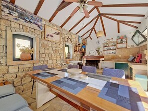 A rustic interior with a stone wall, wooden beams, a dining table with placemats, and a fireplace. - Vacation home Ana by Interhome (Brač/Supetar)