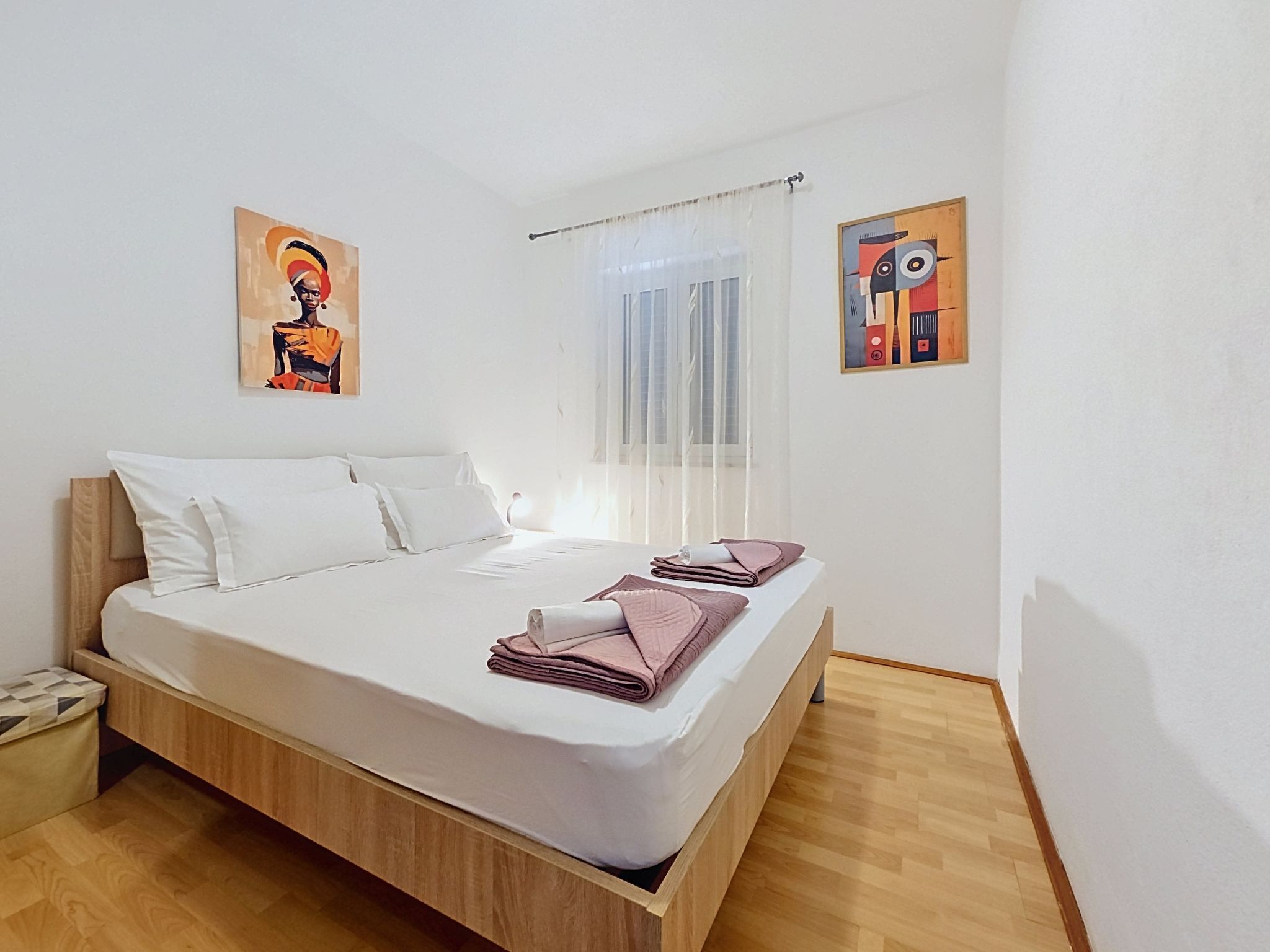 Een moderne slaapkamer met een houten bedframe, wit beddengoed en twee abstracte schilderijen aan de muur.