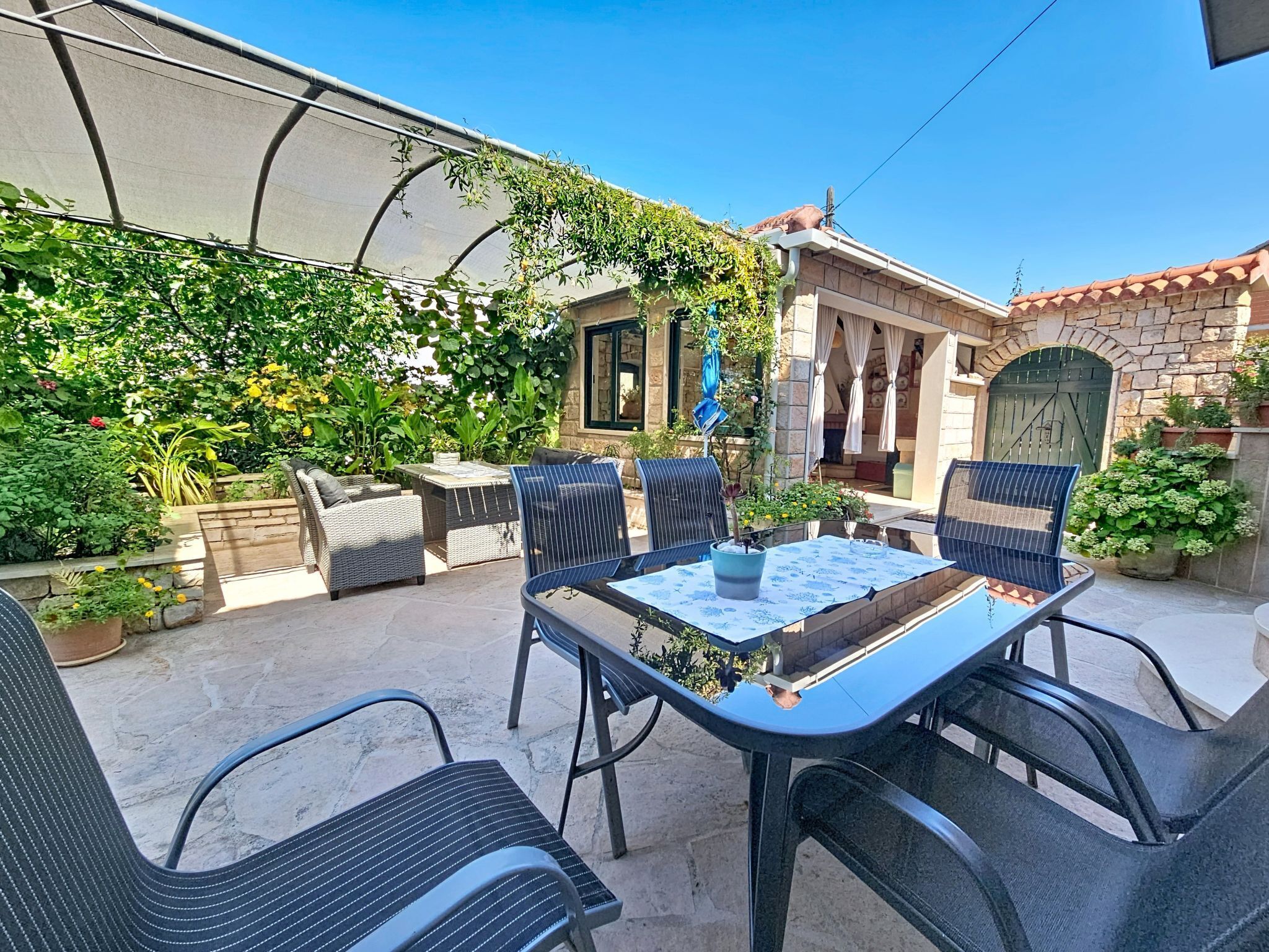 An outdoor patio with a table and chairs, surrounded by greenery and a stone building.