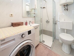 Et moderne badeværelse med vaskemaskine, brusekabine i glas og toilet.