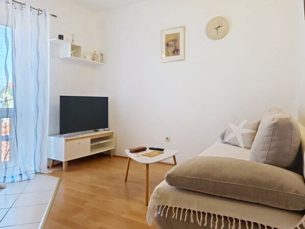 Een woonkamer met een tv op een dressoir, een bank, een bijzettafeltje en een wandklok.