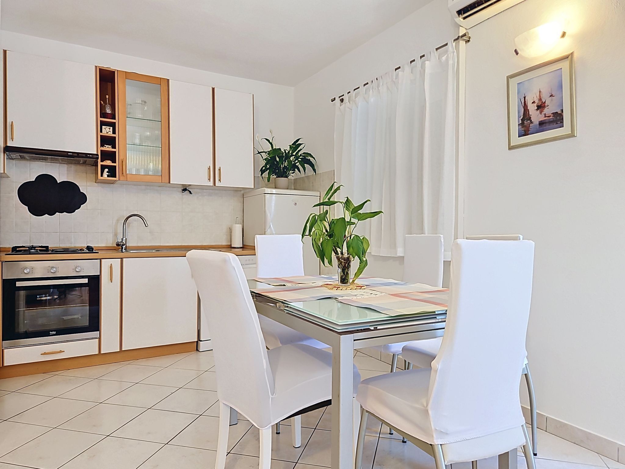 A modern kitchen with white cabinetry, a dining table with chairs, and a potted plant on the counter.