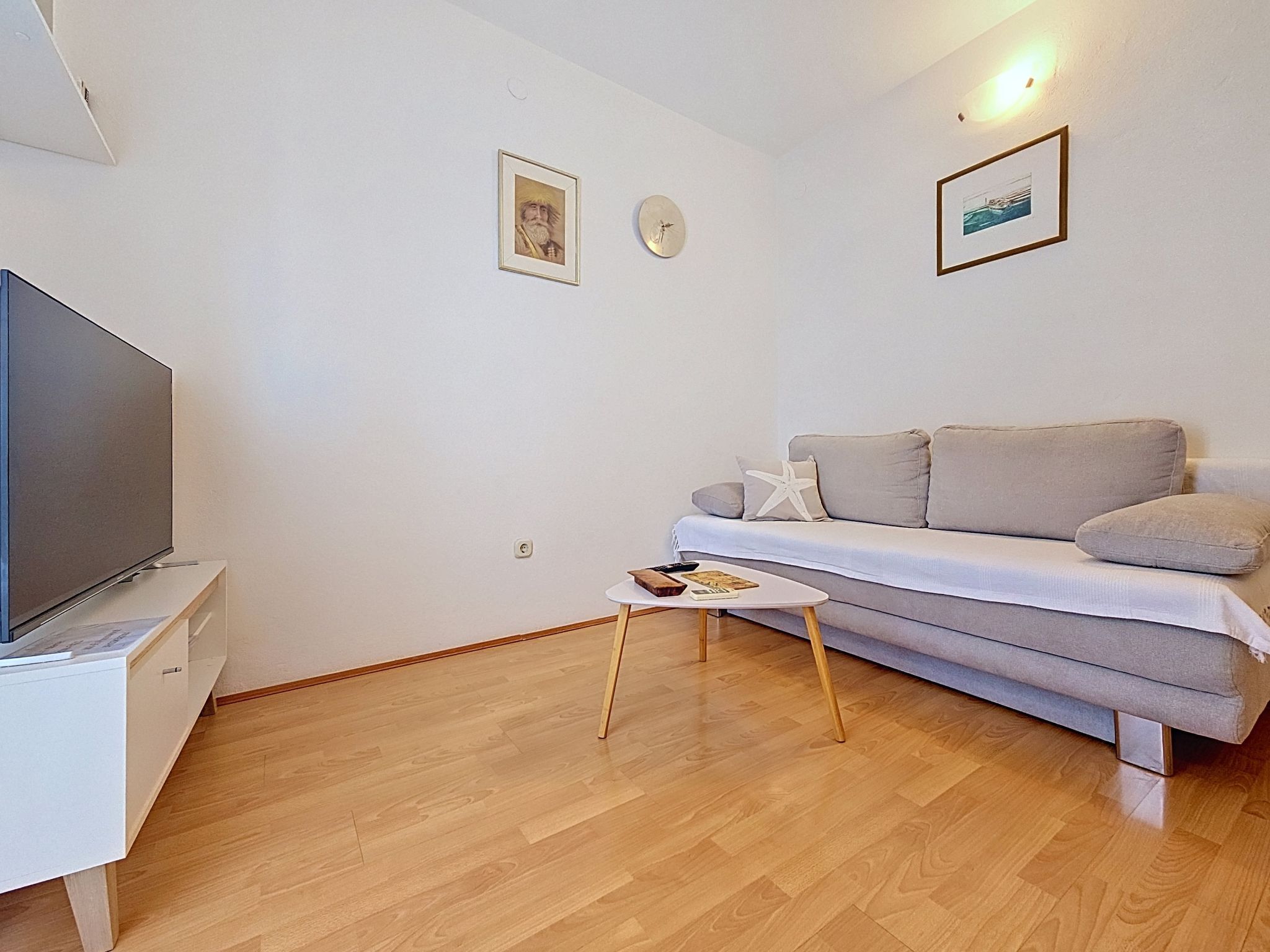 A modern living room with a flat-screen TV, a sofa, a small coffee table, and a wall clock.