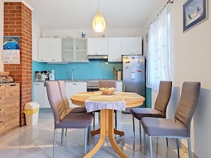 Cocina compacta con armarios blancos, una isla central con sillas, una lámpara colgante y un calendario en la pared.