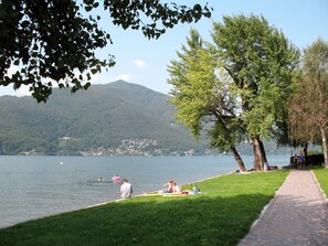 A lakeside park with a paved walkway, grassy areas, and trees.