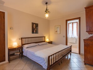 A bedroom with a wooden bed, bedside lamps, a ceiling light, a door with curtains, and a wooden cabinet.