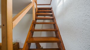 Uma escada de madeira com corrimão, que leva a um patamar com luminária.