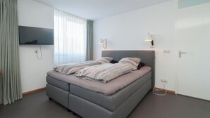 Een moderne slaapkamer met een bed, een flatscreen televisie aan de wand, een bedlamp en een deur met een handgreep.