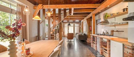 A modern kitchen with wooden beams, a dining area with a wooden table, and a staircase leading to another level.