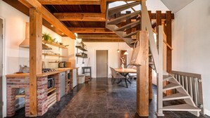 Un intérieur spacieux agrémenté d’une cheminée en briques, de poutres en bois, d’un escalier et d’un coin repas.