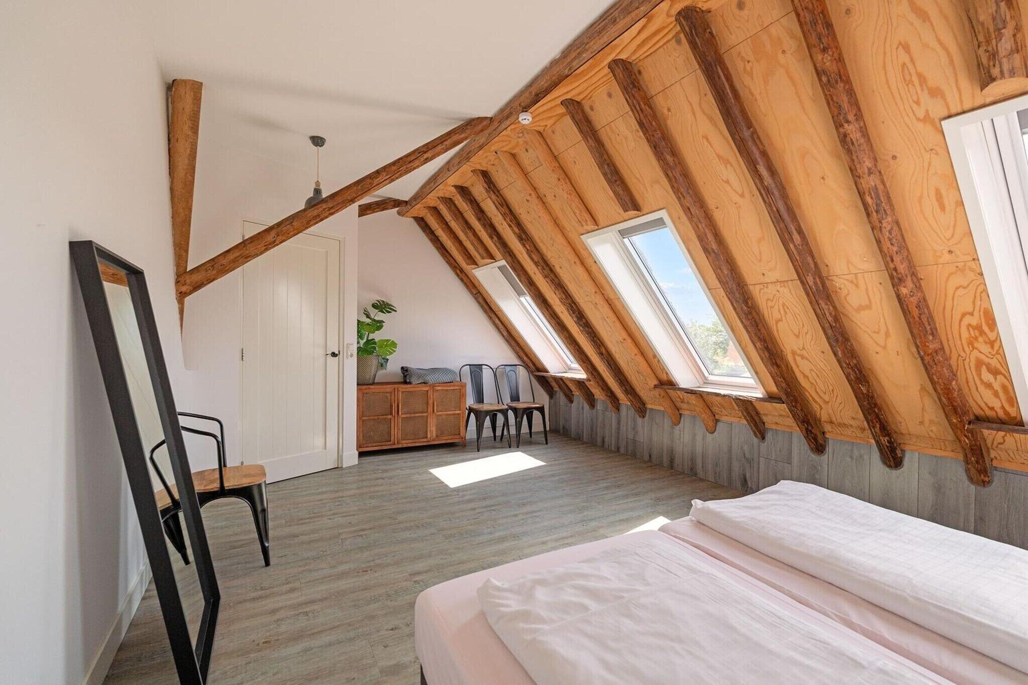 Een kamer met een schuine balkenplafond, een bed, een stoel, een kast en een raam.