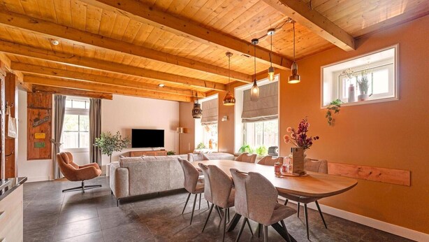 A spacious dining area with a wooden ceiling, a large table, and several chairs.