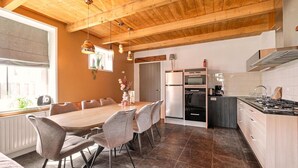 A modern kitchen with a wooden ceiling, a dining area with a round table and chairs, and a view of the outside through a window.