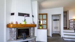 Ein Kamin aus Stein mit hölzernem Sims, einer Topfpflanze und Dekoration. Eine Treppe mit Metallgeländer führt zu einer oberen Ebene.